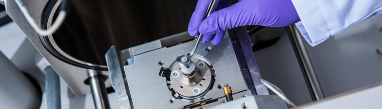 Purple gloved hand adjusting machinery with metal tweezers
